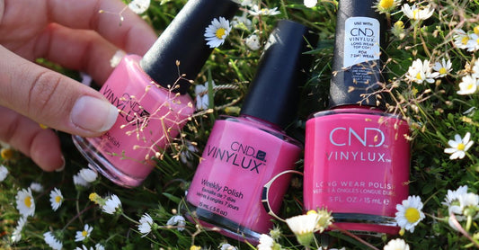 Acrylic Nails vs Gel Nails: Flache Lage von Nagellackflaschen und UV-Lampe auf hellem Hintergrund