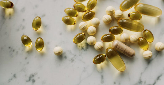 Eine Flasche Vitamin-D-Kapseln auf einem weißen Tisch, daneben ein Glas Wasser.