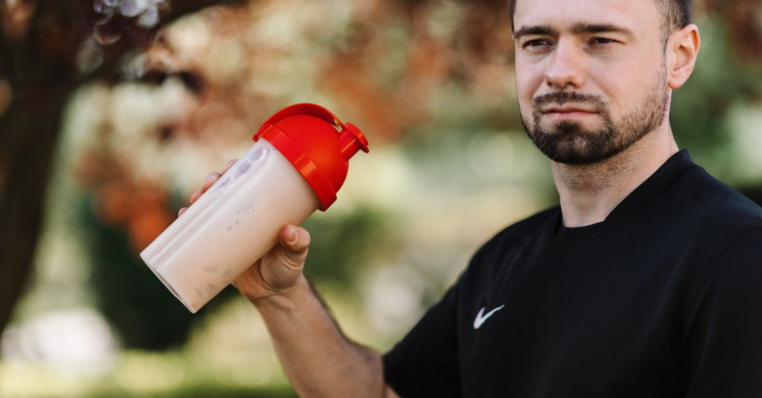 Ein Glas mit cremigem Casein-Protein-Shake auf einem Nachttisch, daneben ein Messlöffel und eine Packung Casein-Protein-Pulver – ideal für den Verzehr vor dem Schlafengehen.