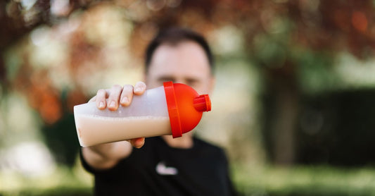 Ein Messlöffel mit feinem, weißen Whey-Protein-Pulver auf einer dunklen Holzoberfläche, daneben ein Shaker. Symbolbild für den Whey Protein Isolate vs Concentrate Vergleich.