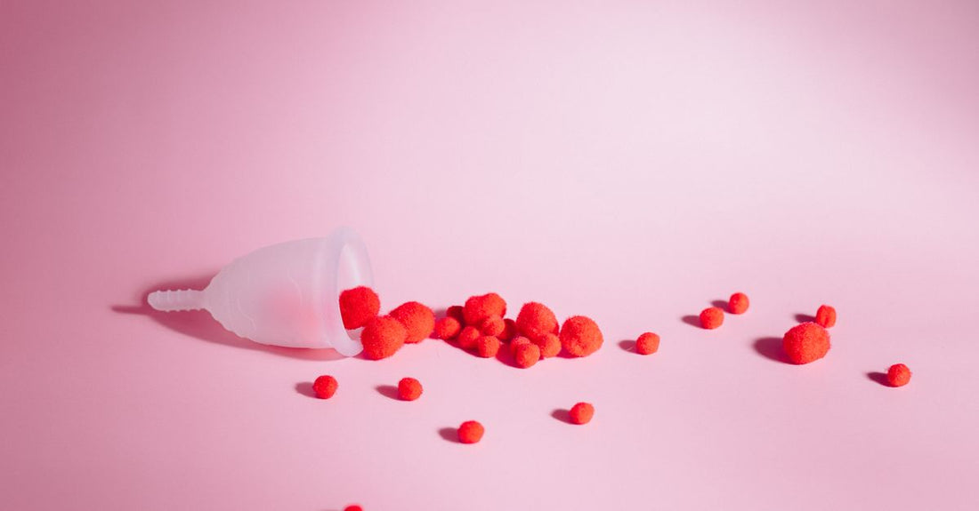 Eine weiche, transparente Menstruationstasse aus medizinischem Silikon neben einem Bio-Baumwoll-Tampon auf einem neutralen Hintergrund – Menstruationstasse vs. Tampons Vor- und Nachteile
