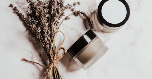 Ein Glas-Tiegel mit Sleeping Mask auf einem weißen Marmortisch, umgeben von grünen Blättern – how to choose sleeping masks
