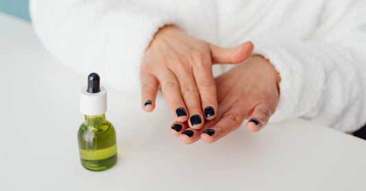 Flaschen mit Nagelhautöl für gesunde Nägel, umgeben von natürlichen Inhaltsstoffen wie Jojoba und Vitamin E auf einem hellen Holzuntergrund.