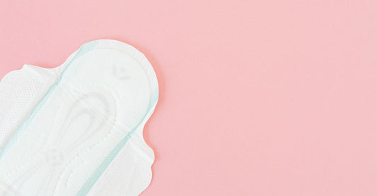 Sanitary Napkins Buying Guide: Verschiedene Damenbinden auf einem Holztisch ausgebreitet, mit Baumwollblüten dekoriert.