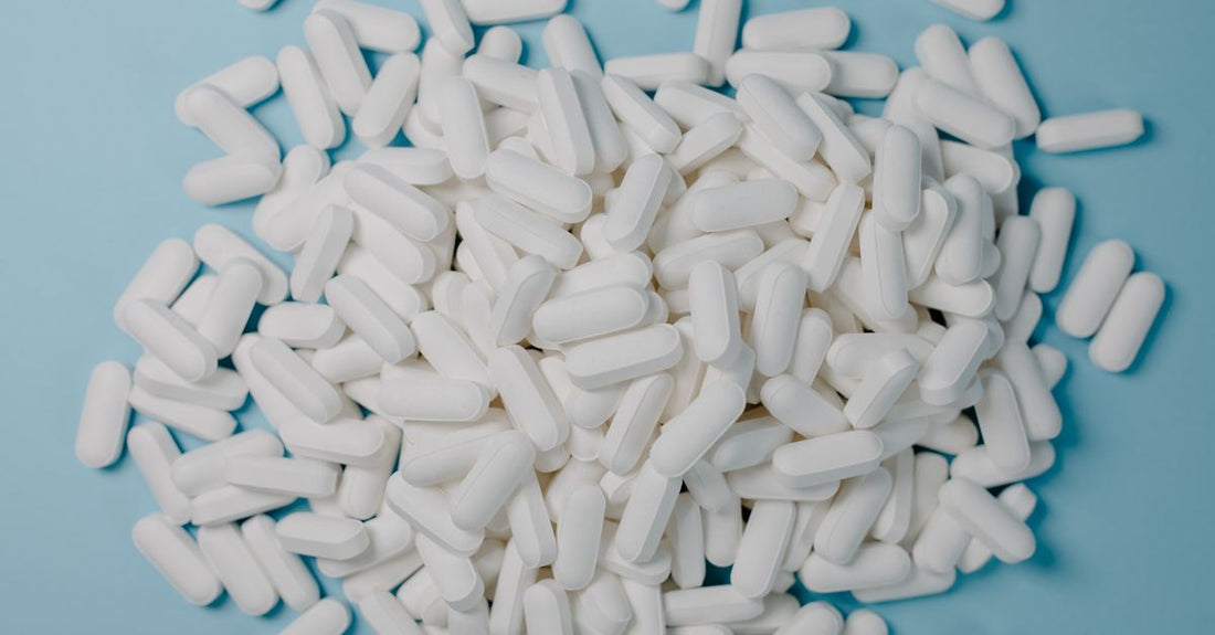 PCOS Supplements für Hormonbalance: Flasche mit Inositol-Kapseln auf einem Holztisch, daneben ein Glas Wasser und eine frische Blume.