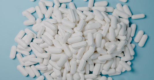 PCOS Supplements für Hormonbalance: Flasche mit Inositol-Kapseln auf einem Holztisch, daneben ein Glas Wasser und eine frische Blume.