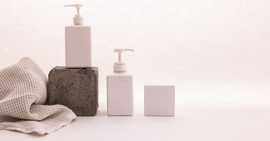Ein moderner Pump Dispenser aus Edelstahl auf einer weißen Badezimmerablage, daneben eine Glasflasche mit Lotion. Perfekt für die Auswahl des richtigen Spenders.